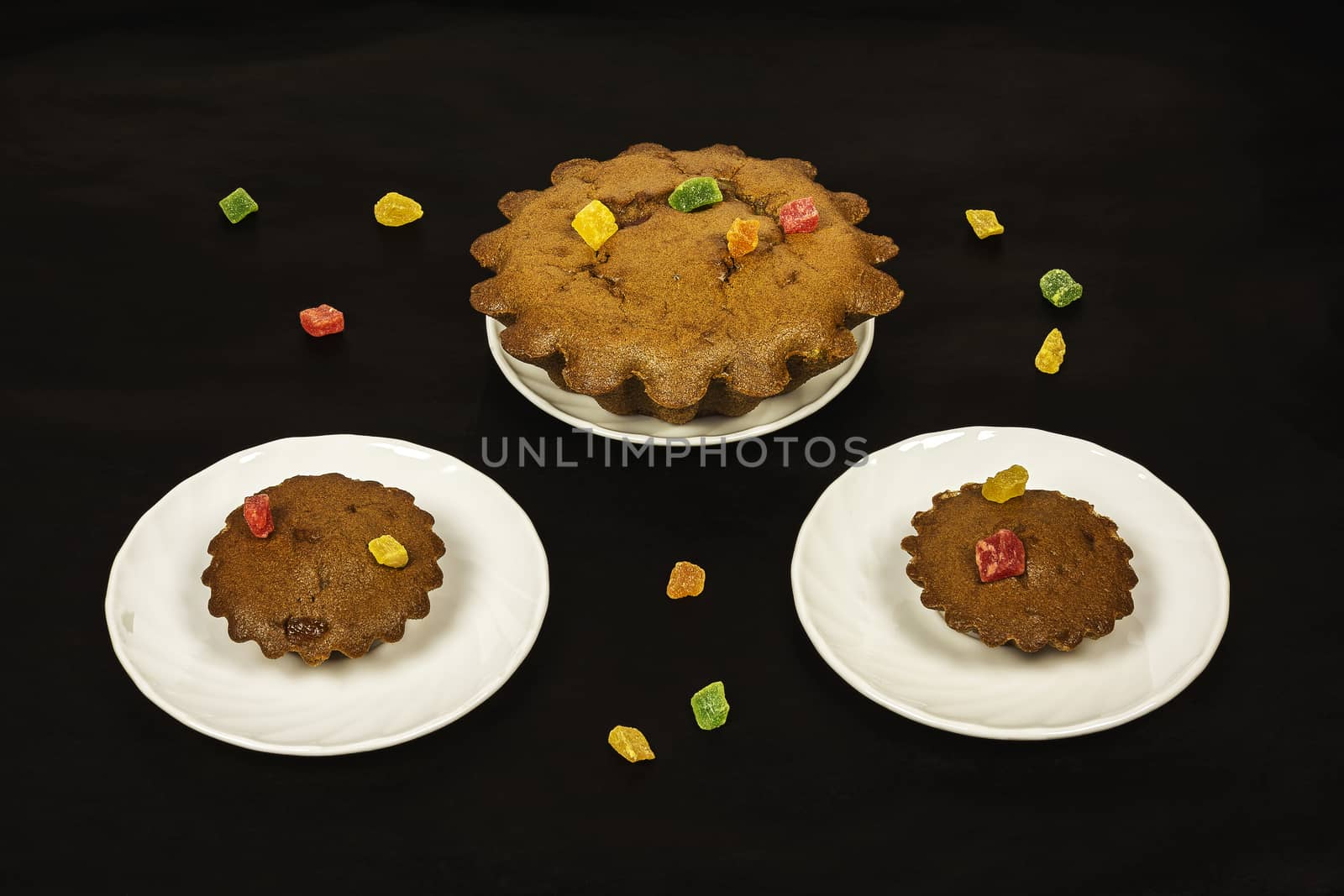 On a dark background there are white saucers with chocolate cakes and candied fruits