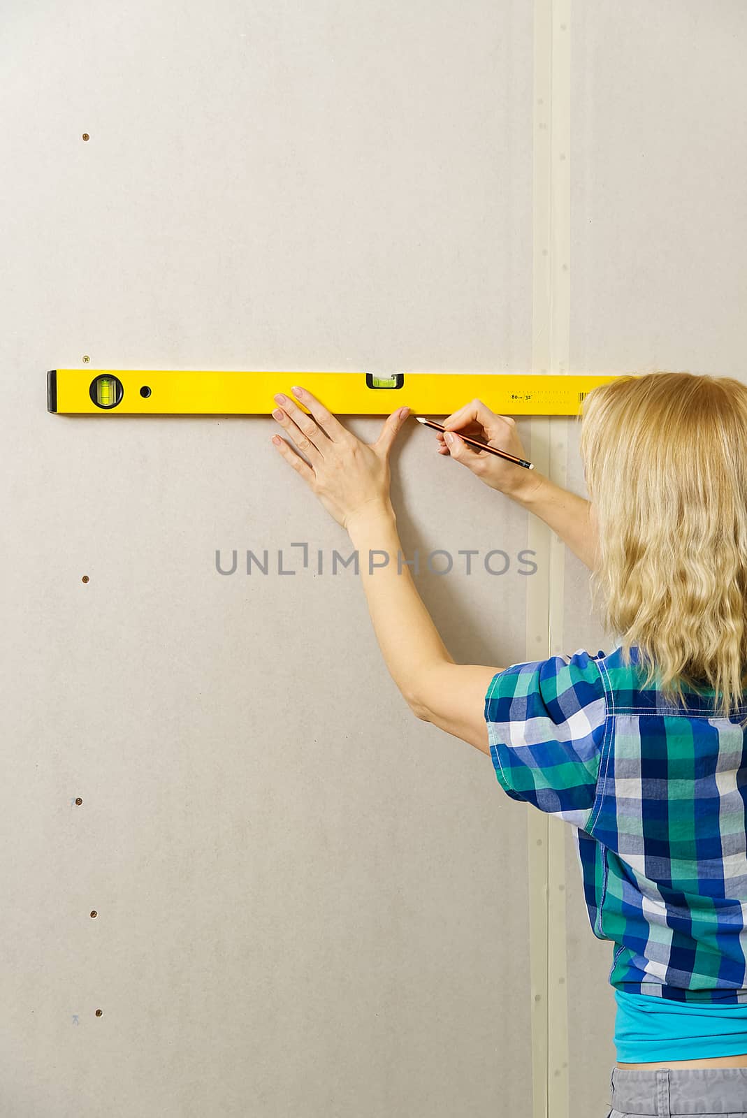 DIY blond young attractive woman using spirit level to work out measurements on plasterboard wall. by PhotoTime