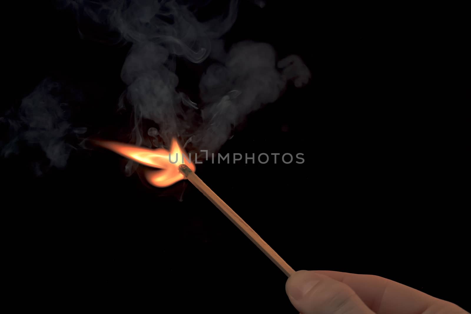 Hand holding a lighted match with fire flame and smoke on a black background.