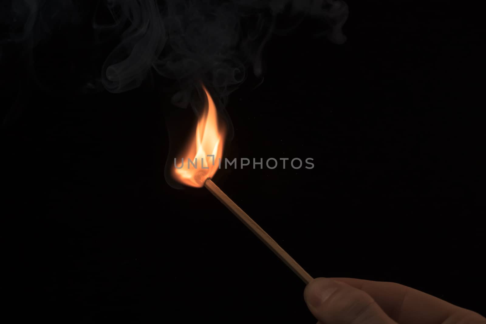 Hand holding a lighted match with fire flame and smoke on a blac by YevgeniySam