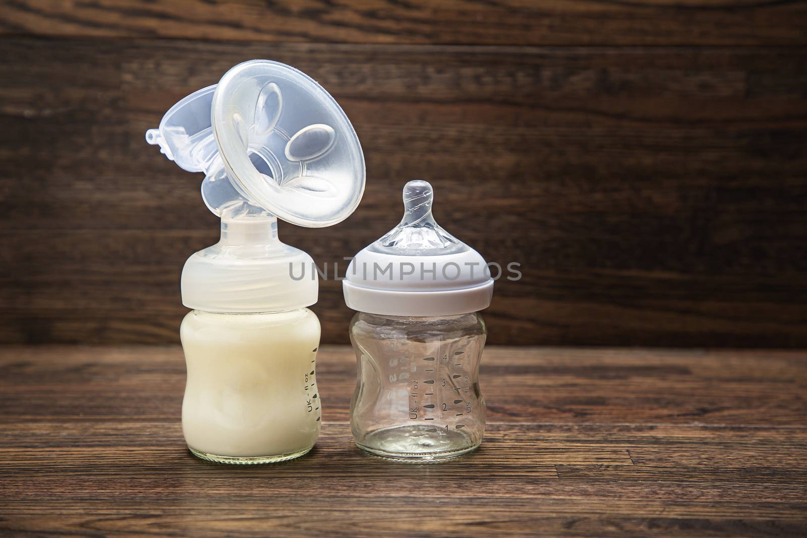 Baby bottle with breast pump attachement and empty bottle against a wood background