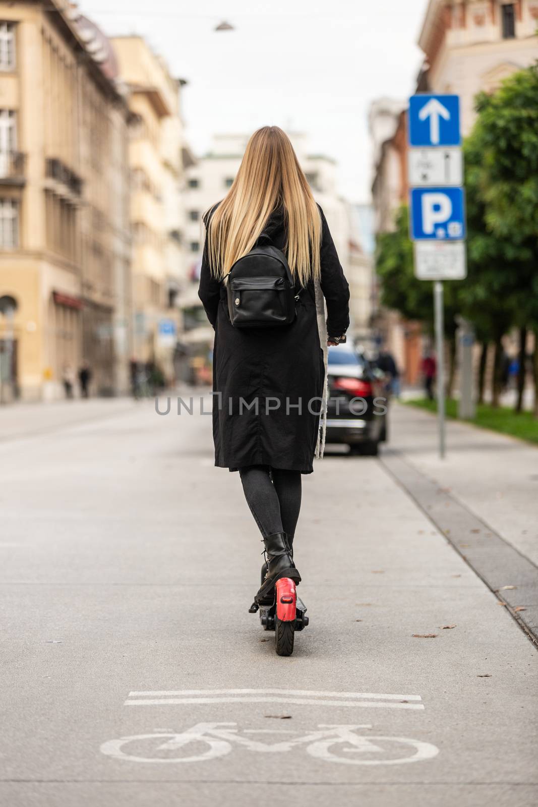 Rear view of girl riding public rental electric scooter in urban city environment. New eco-friendly modern public city transport in Ljubljana by kasto