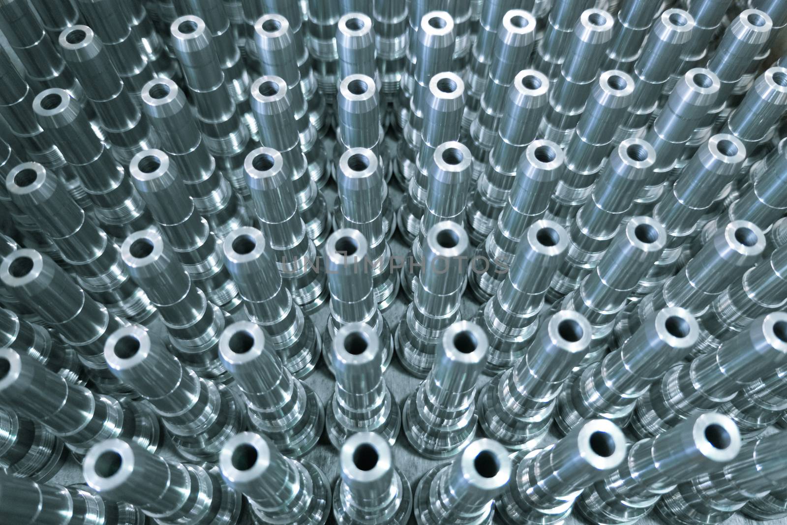 Shiny long steel parts full frame background, clean steel threaded rods after fine cnc turning. Standing vertically in a rows with selective focus and blur.