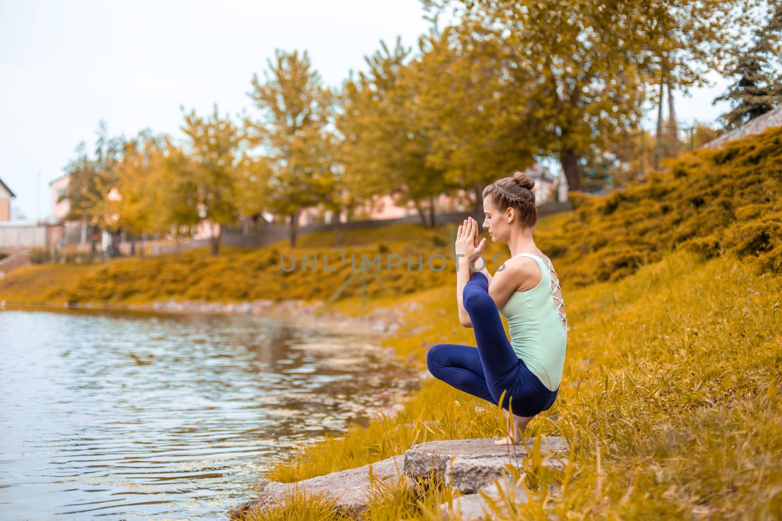 A young sports girl practices yoga on a fall yellow lawn by the river, use yoga assans posture. Meditation and unity with nature.
