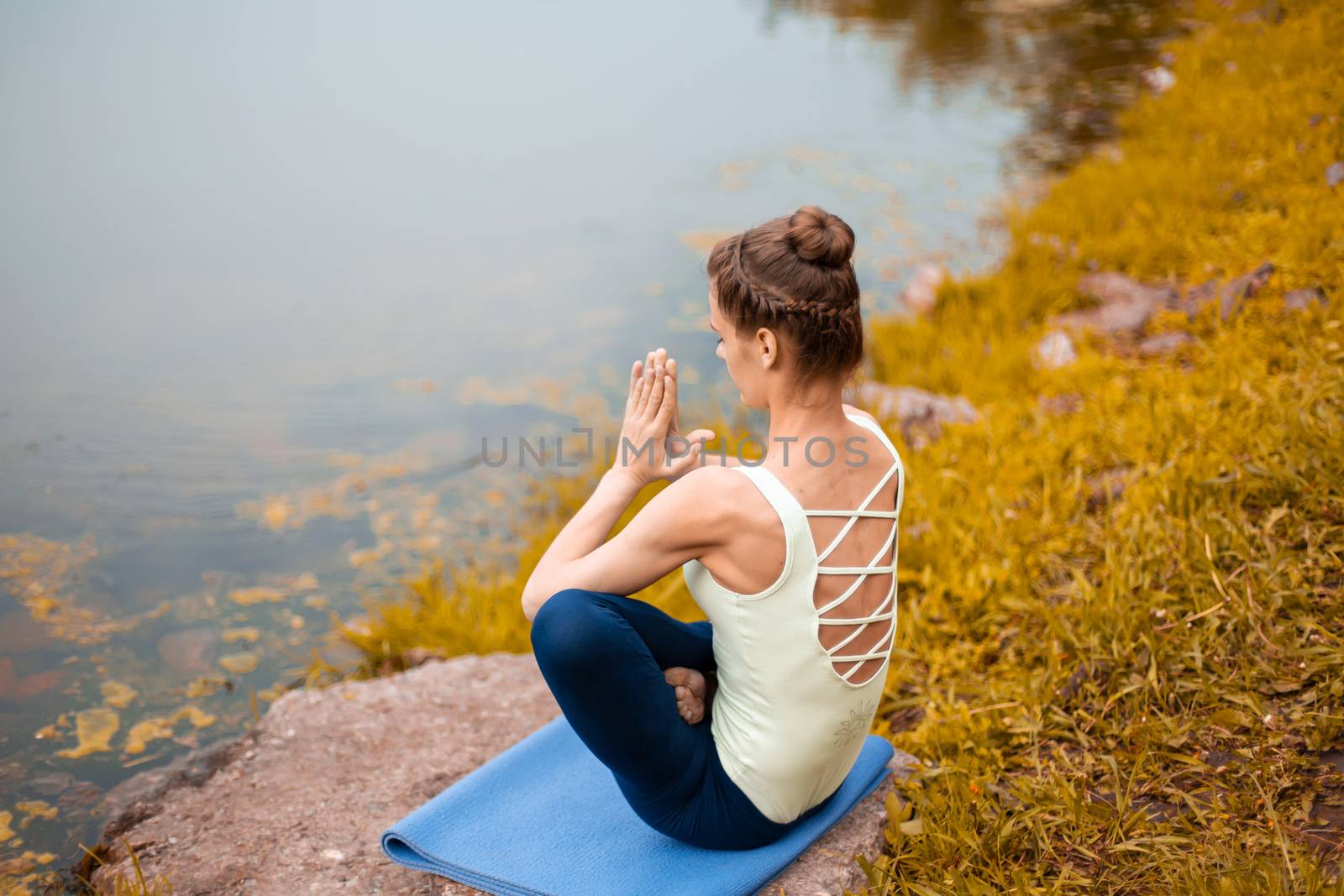 A young sports girl practices yoga on a fall yellow lawn by the river, use yoga assans posture. Meditation and unity with nature.