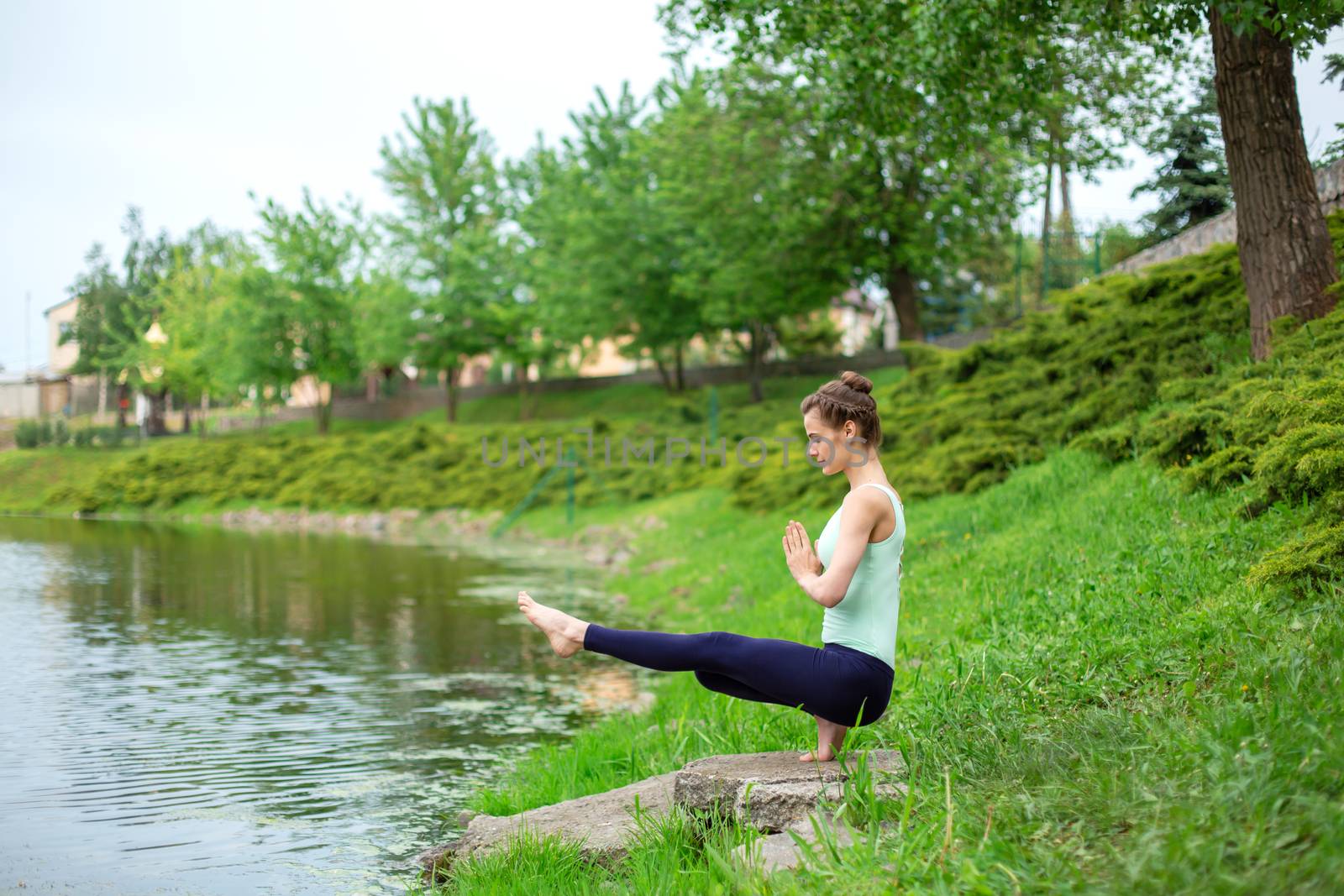 Slim brunette girl doing yoga in the summer on a green lawn by the lake.