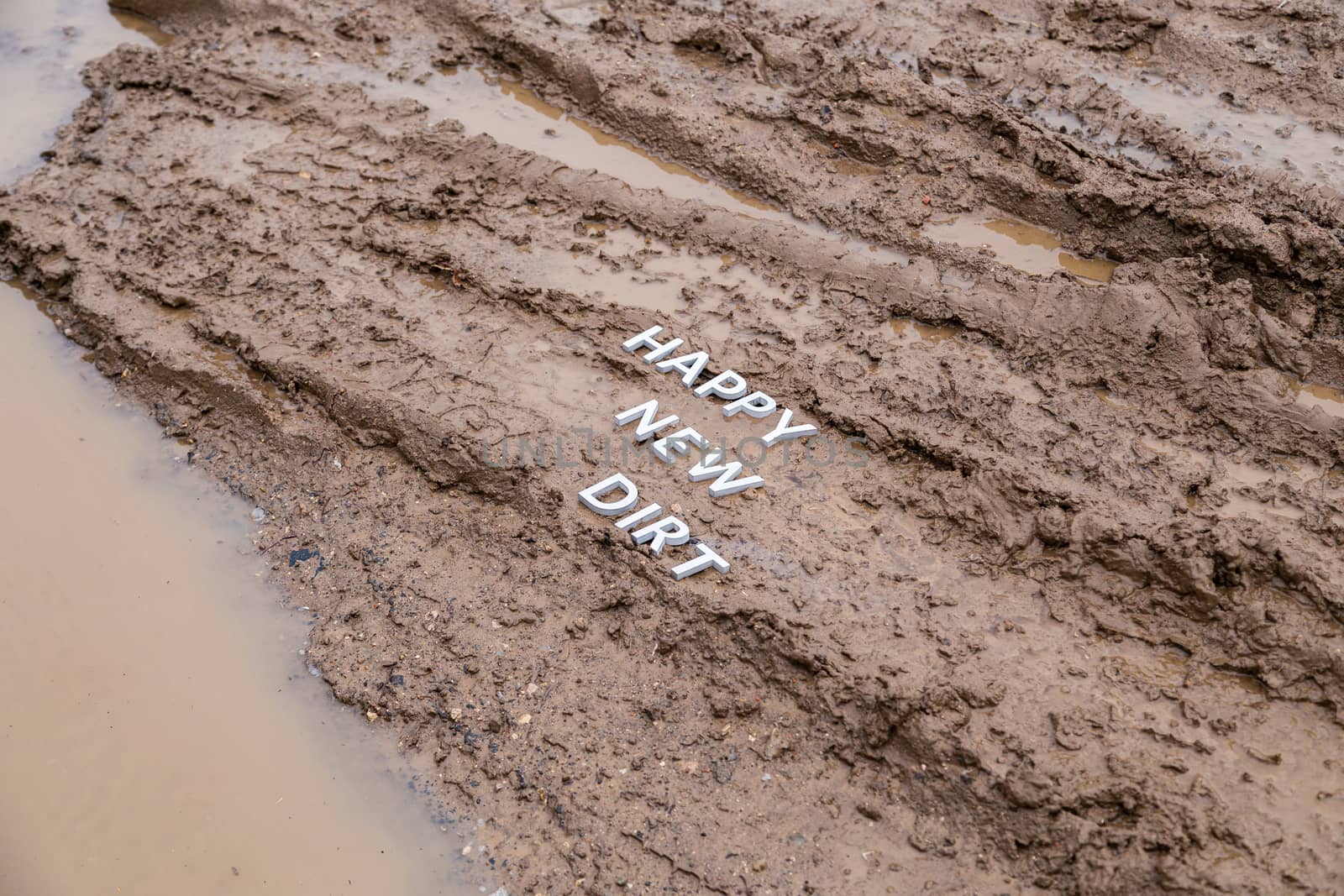 the words happy new dirt laid with silver metal letters on wet mud surface in diagonal perspective under cloudy autumn day light