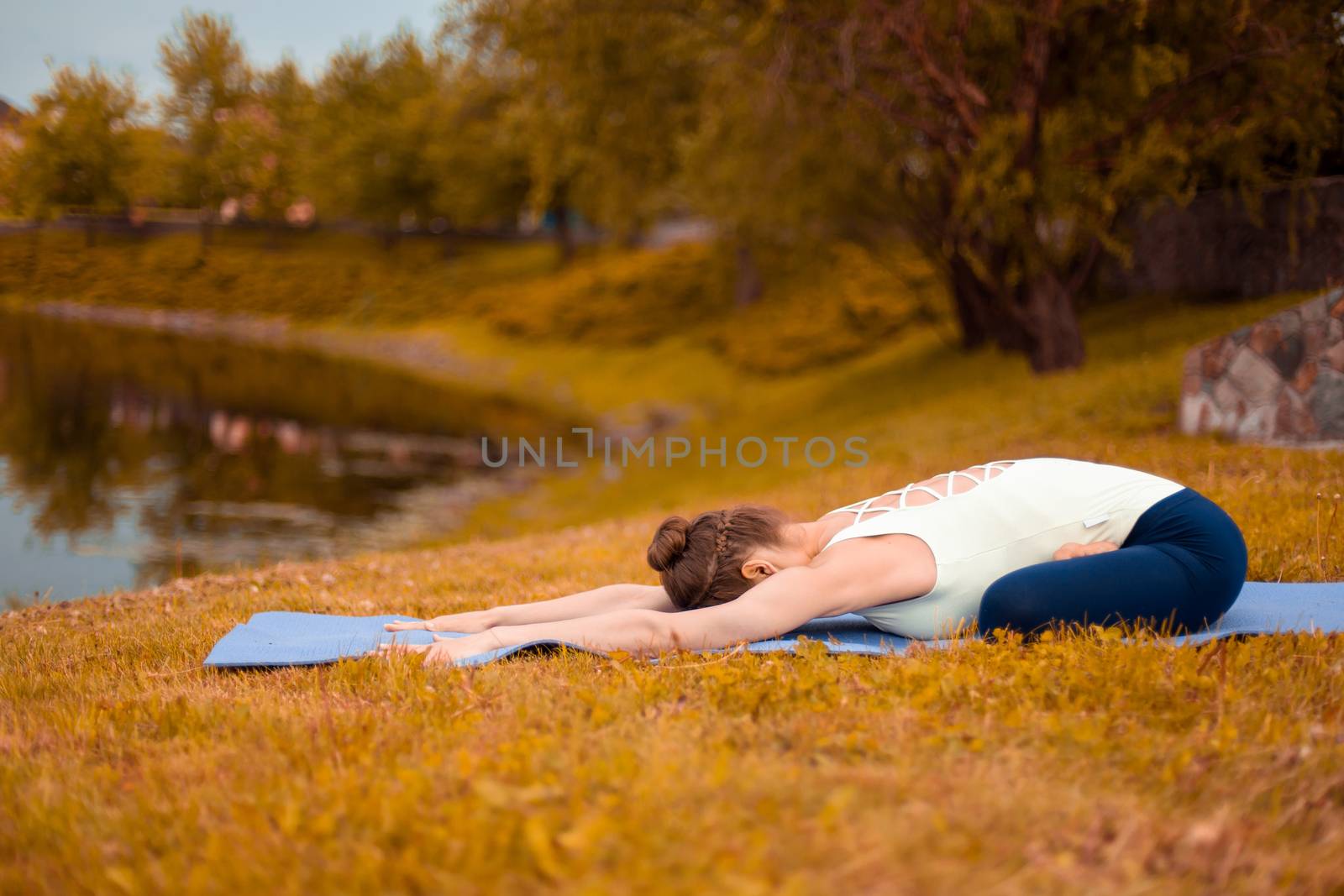 Slim brunette girl goes in for sports and performs yoga poses in the fall in nature by the lake.
