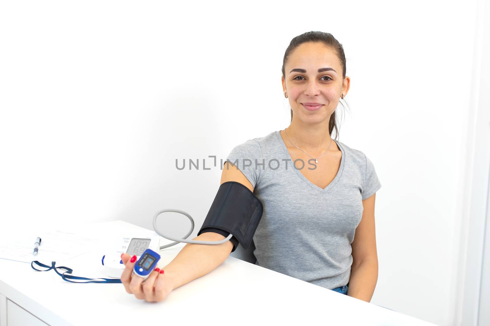 A young girl examined by a doctor, sitting on a chair with connected heart rate sensors and a tonometer.