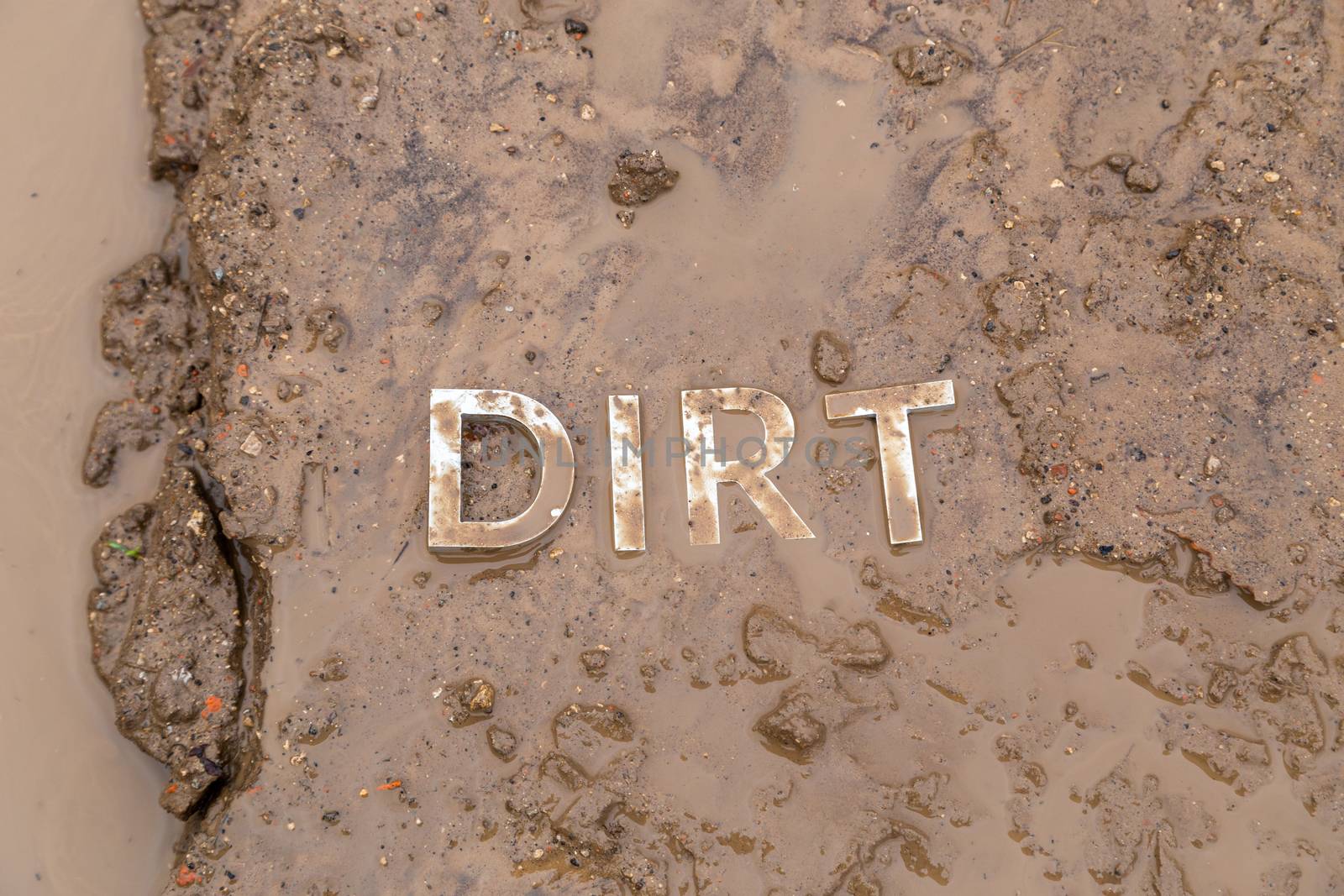the word mud imprinted in wet dirt road surface and puddle - close-up with selective focus in flat lay perspective.