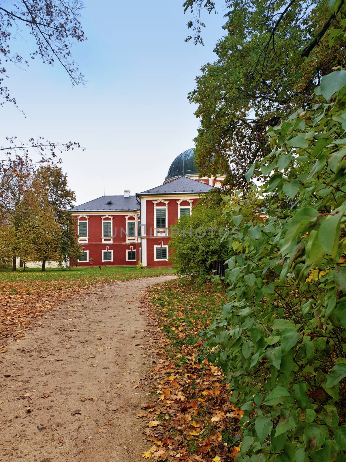 A view of part of beautiful baroque Veltrusy state castle through leaves of bush and path in autumn season.