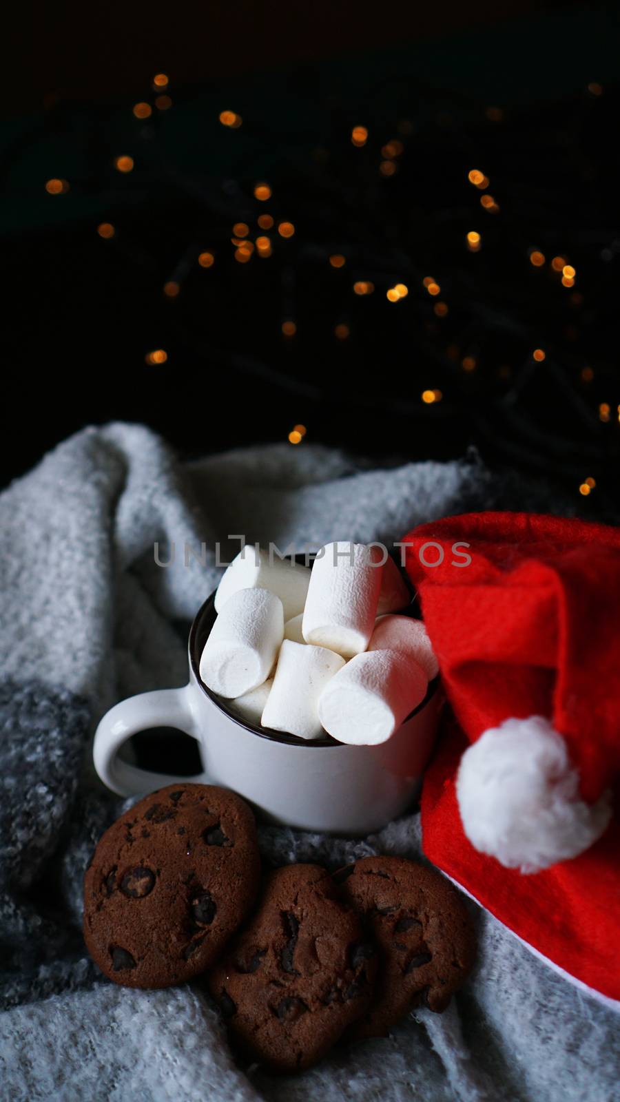 Mug of hot chocolate with christmas hat, marshmallow and chocolate cookies. Christmas spirit, hot winter drink. Selective focus - vertical photo