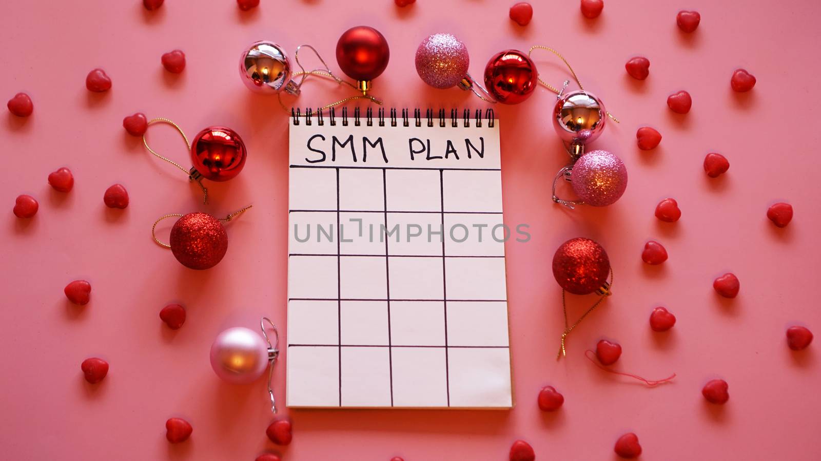 Freelance project. SMM plan blank. White sheet on a pink festive background with red Christmas balls and candy in the form of hearts