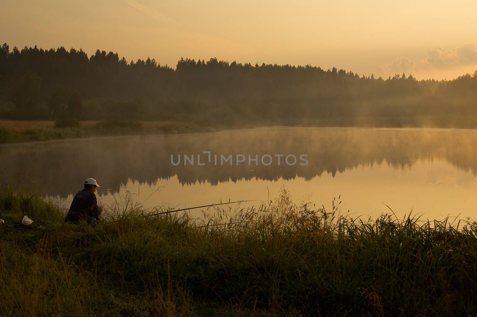 A fisherman at sunset on the pond catches fish.