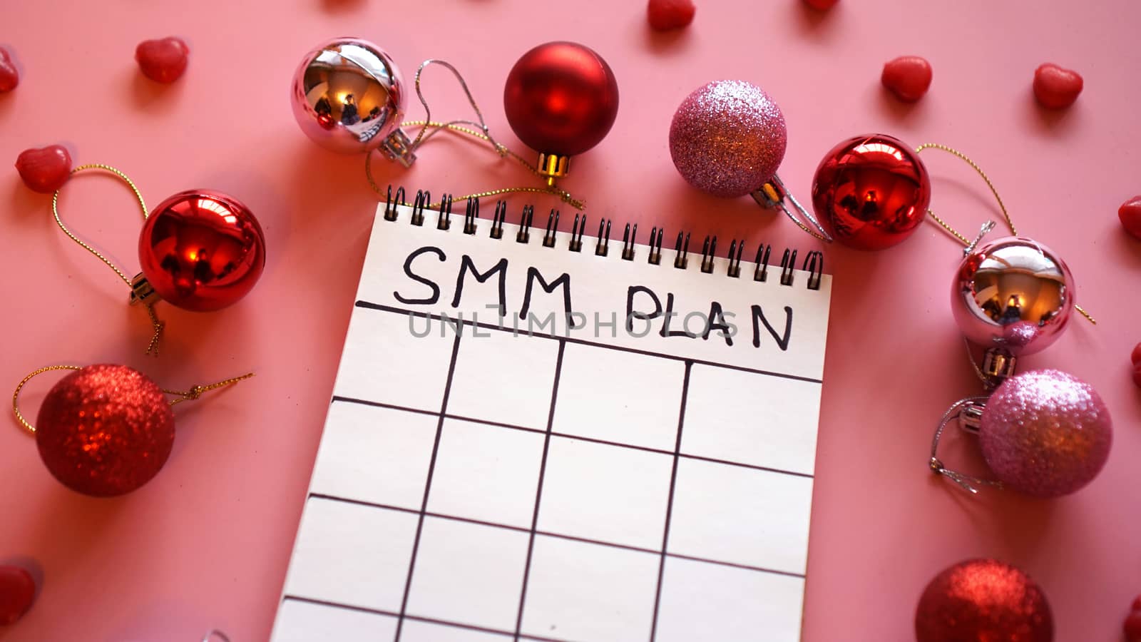 Freelance project. SMM plan blank. White sheet on a pink festive background with red Christmas balls and candy in the form of hearts