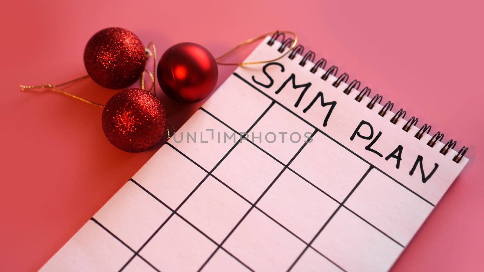 Freelance project. SMM plan blank. White sheet on a pink festive background with red Christmas balls