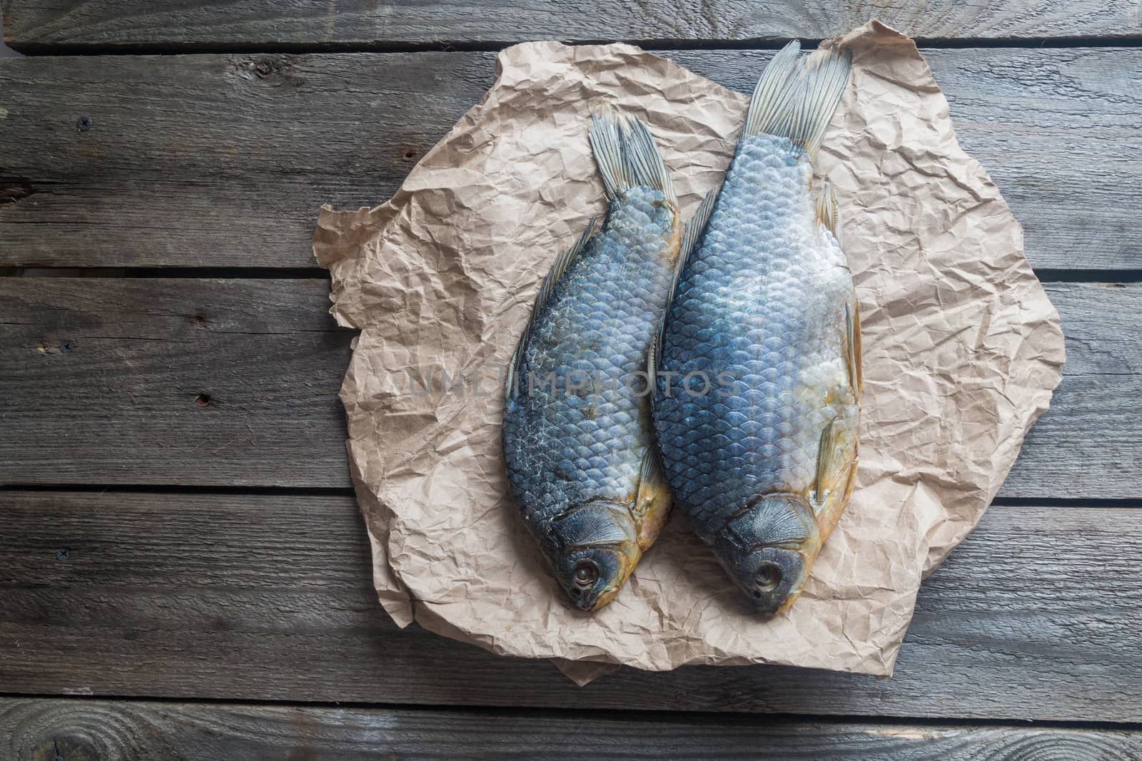 Salted Dry fish vobla on crumpled craft paper on wooden background, delicious beer snack, close-up.