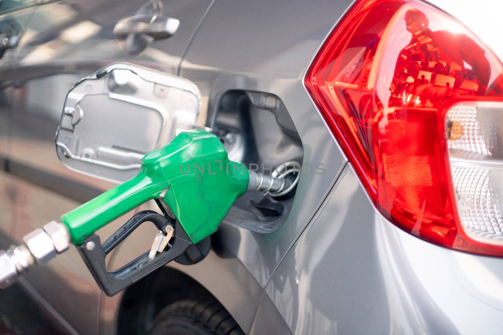 Man at a petrol pump fuel station inserting nozzle into fuel tank of a car and starting the fuel pumping in the auto cut off petro diesel pump by Shalinimathur