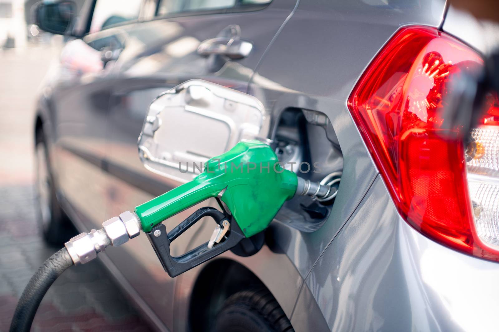 Man at a petrol pump fuel station inserting nozzle into fuel tank of a car and starting the fuel pumping in the auto cut off petro diesel pump. Shows the high dependence of india on fossil unleaded fuels shown by the green nozzle as this non renewable environment friendly fuel is replaced by cheaper alternatives