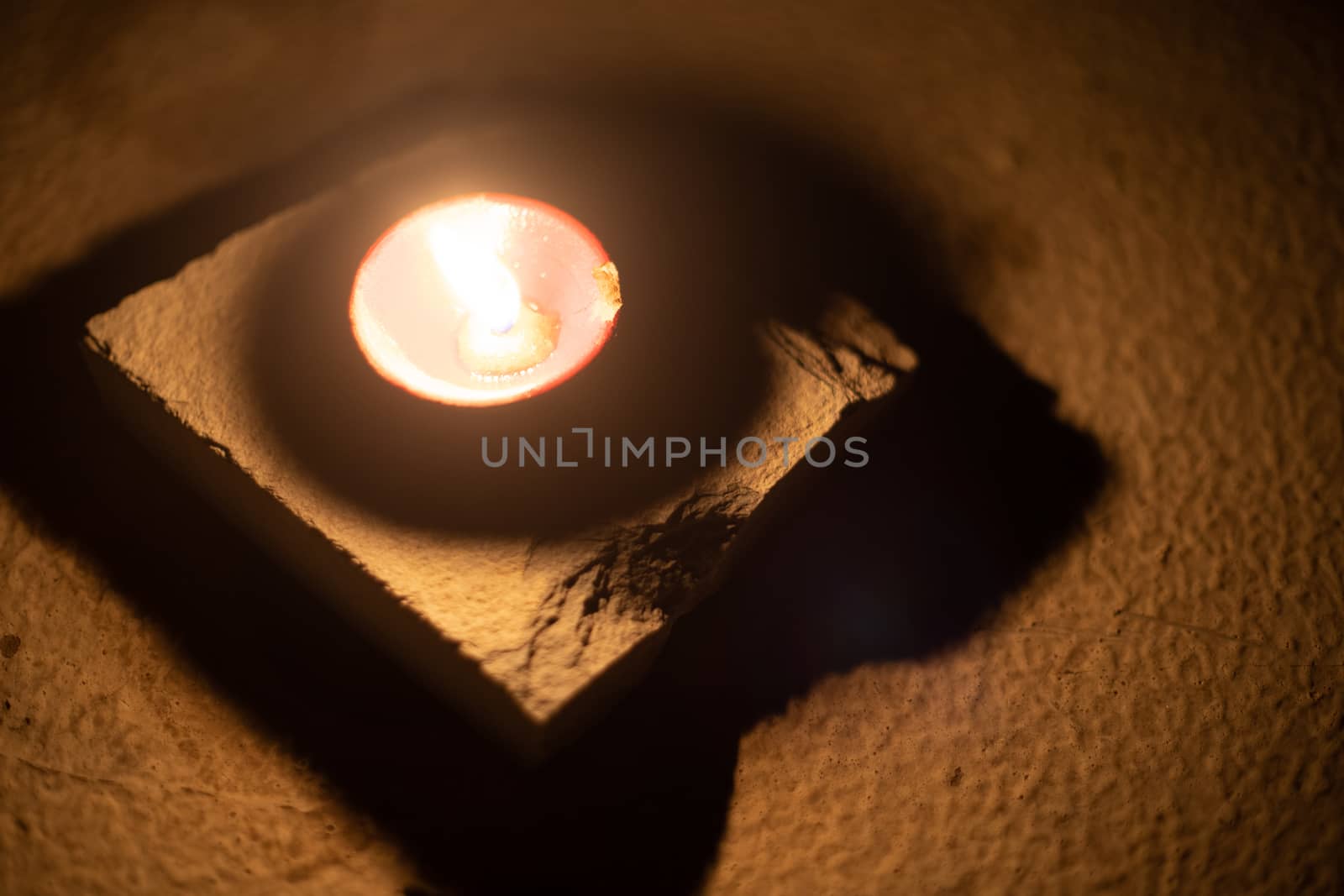 Top down shot showing a diya oil lamp filled with oil and a cotton wick burning placed in a dark room chasing away darkness with it's light on the hindu festival of diwali dussera by Shalinimathur