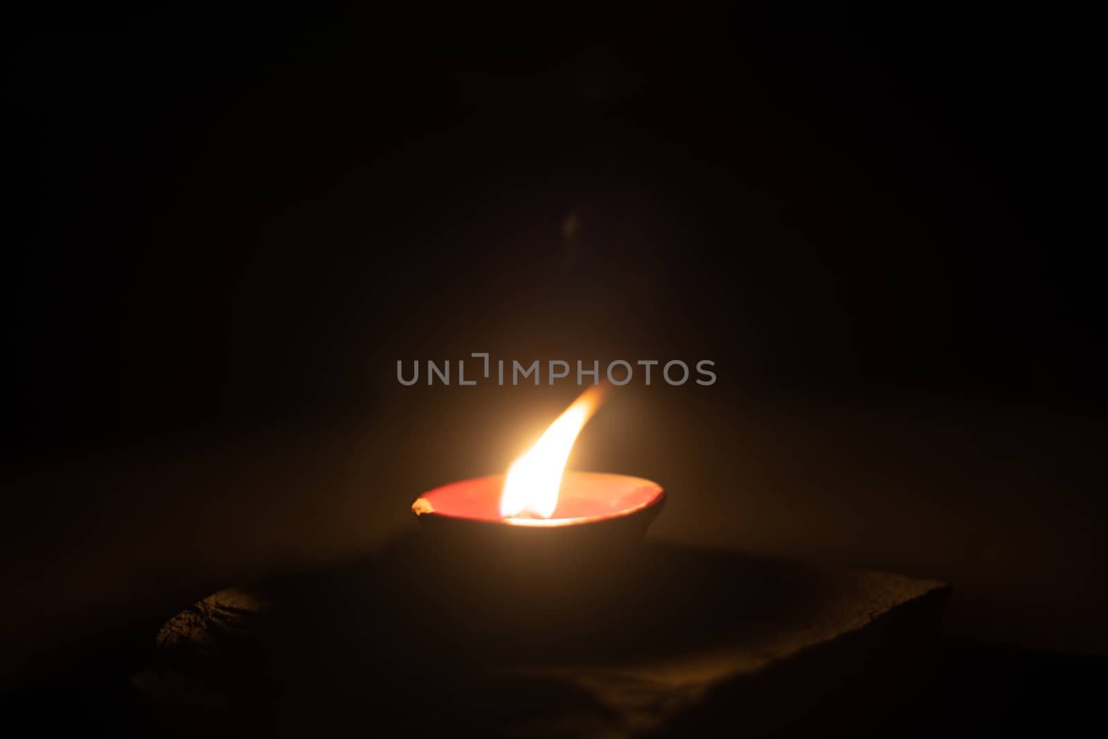 dark minimalistic image showing a diya oil lamp filled with oil or ghee and burning a cotton wick to produce a flame, its a popular religious item and decoration item on the hindu festival of diwali by Shalinimathur