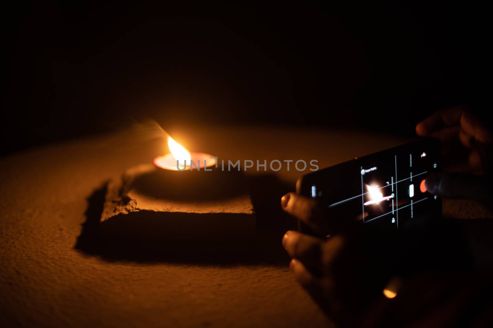 Man woman taking low light pictures of a diya oil lamp with a mobile phone for sharing images on the hindu festival of diwali by Shalinimathur