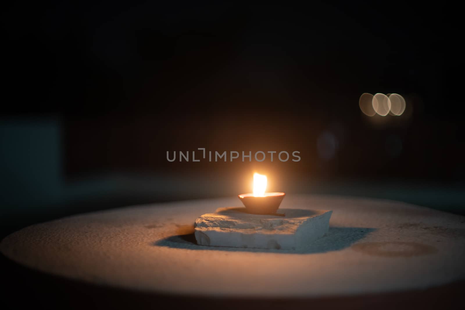 dark minimalistic image showing a diya oil lamp filled with oil or ghee and burning a cotton wick to produce a flame, its a popular religious item and decoration item on the hindu festival of diwali by Shalinimathur