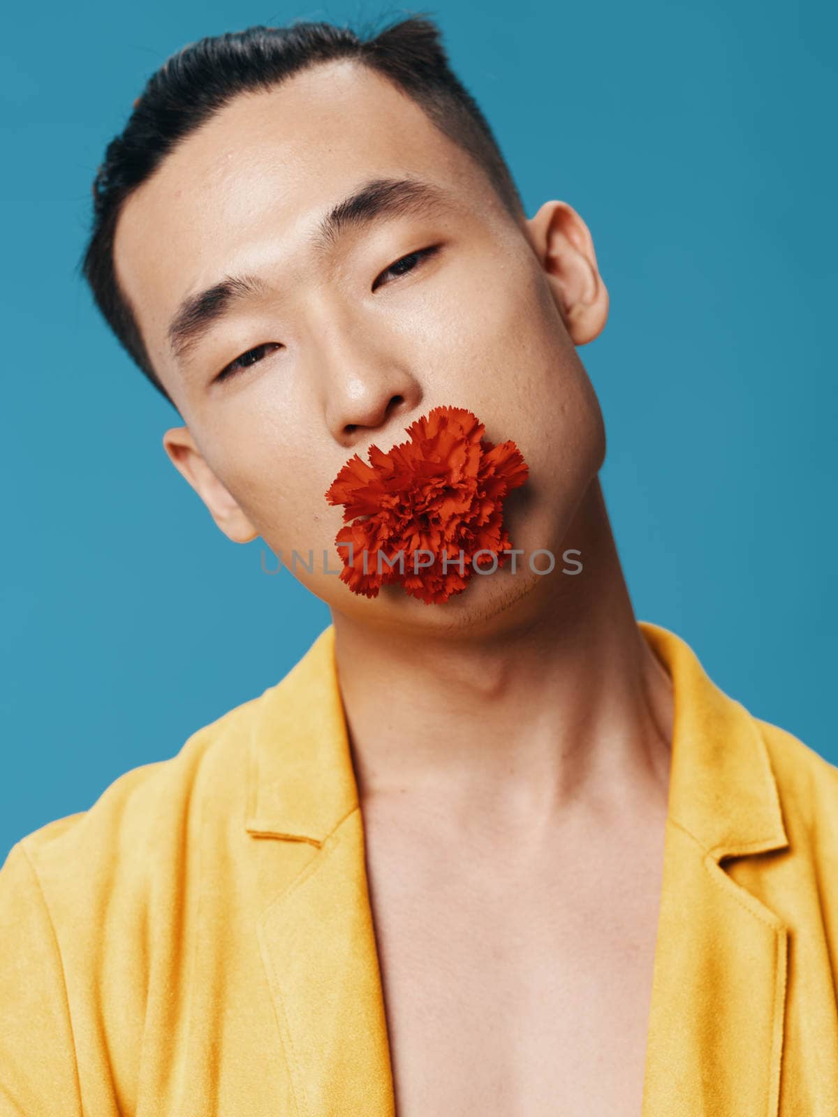 A man in a yellow coat with a red flower in his mouth on a blue background Asian appearance. High quality photo
