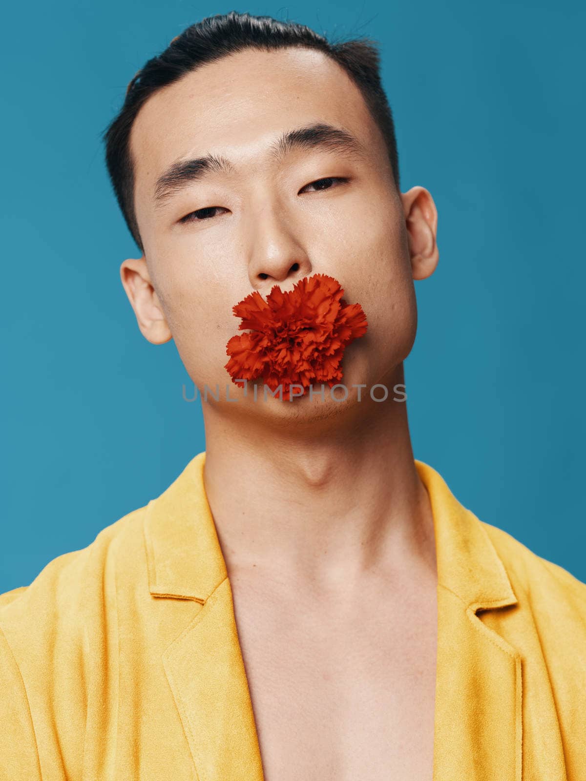 A man in a yellow coat with a red flower in his mouth on a blue background Asian appearance portrait. High quality photo