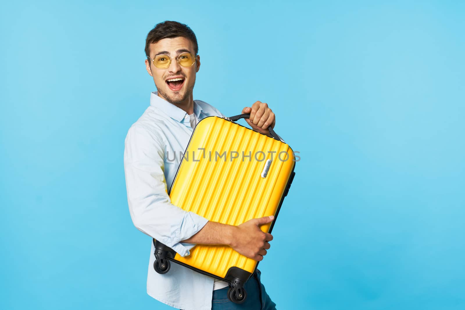 A man in glasses with a suitcase in his hands with a wide open mouth looks ahead on a blue background