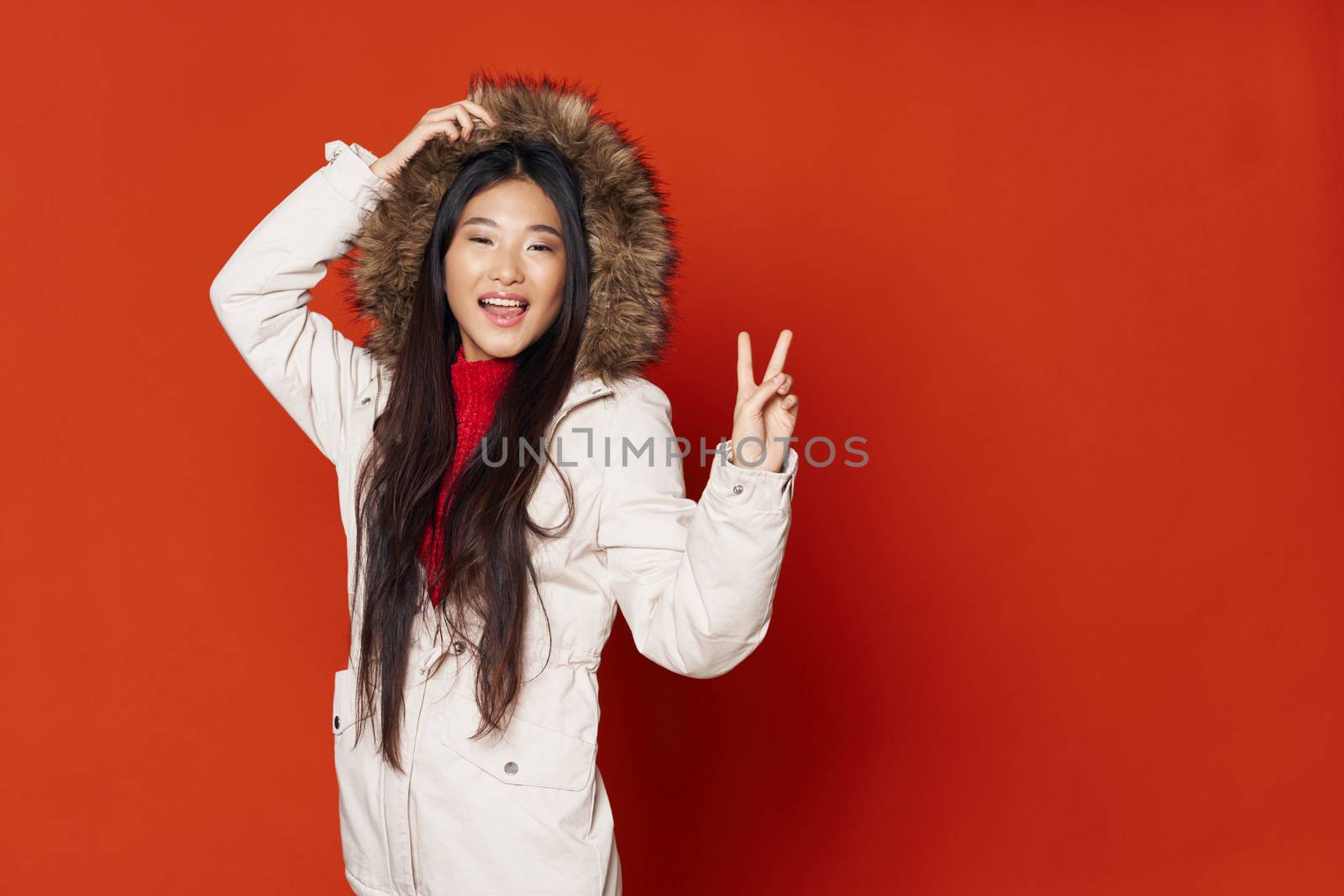 Woman white winter jacket with a hood gestures with a hand red background