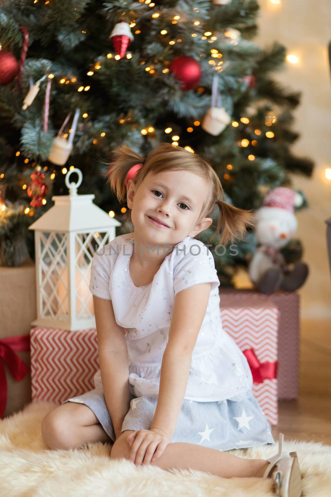 Pretty little child is sitting in front of christmas tree among garlands by galinasharapova
