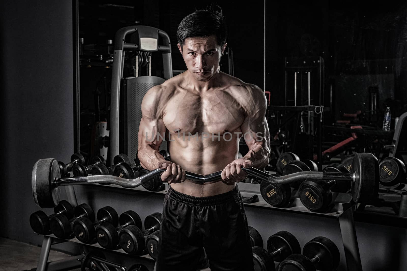 Strong fitness man doing arm workout with barbells in the gym