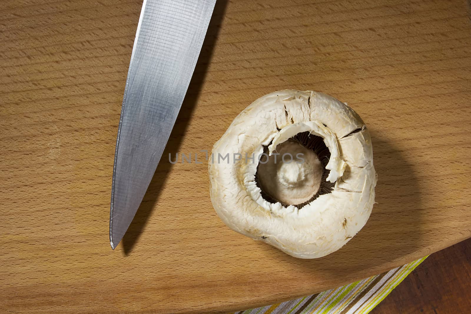 Raw champignon mushroom cap and knife on wooden cutting board