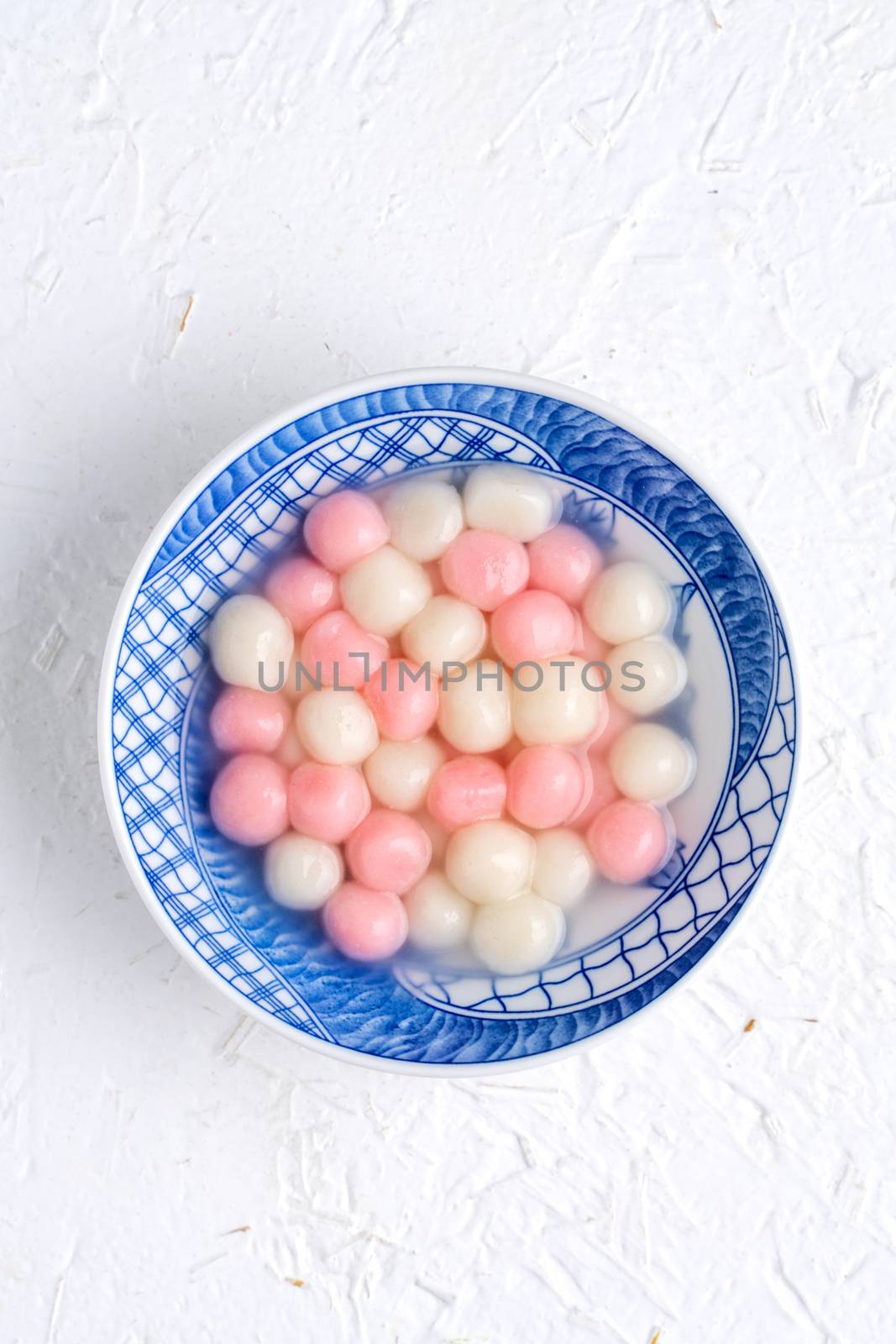 Top view of red and white tangyuan (tang yuan, glutinous rice dumpling balls) in blue bowl on white background for Winter solstice festival food.