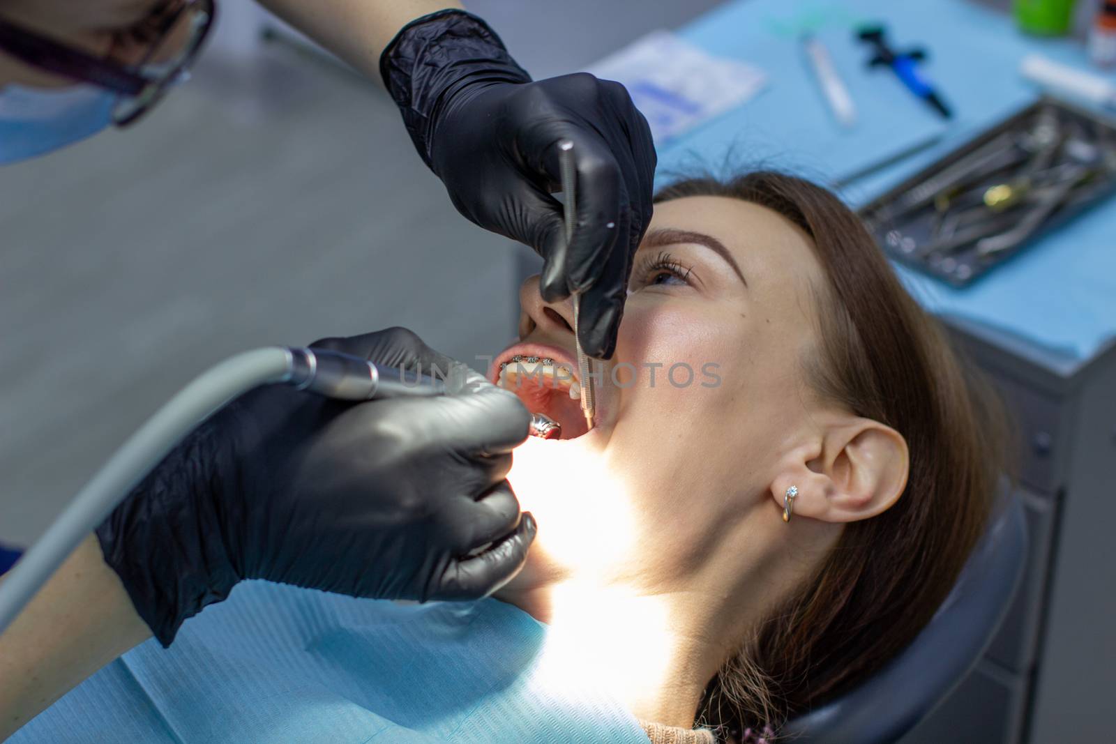 Beautiful woman in dental chair during procedure of installing braces to upper and lower teeth. Dentist and assistant working together, dental tools in their hands. Top view. Concept of dentistry