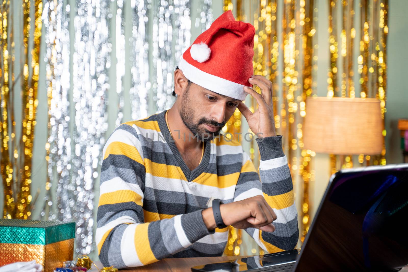 young man with busy working on laptop and watching as late night time during Christmas or new year eve - Concept of work from home during holiday season due to coronavirus or covid-19 pandemic by lakshmiprasad.maski@gmai.com
