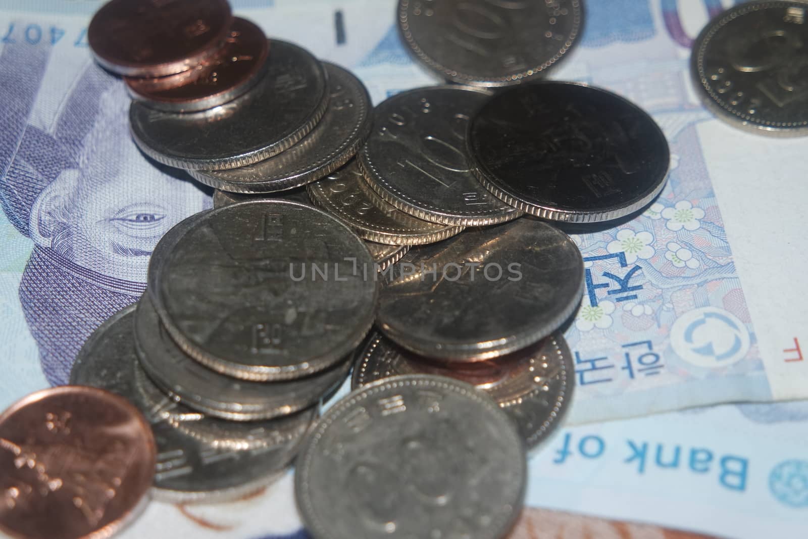 Korean won coins scattered over Korean notes on a wooden floor by Photochowk