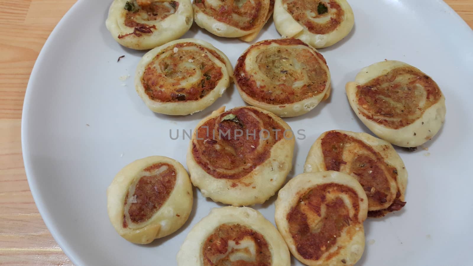Closeup of delicious home made pinwheel puff pastries food item placed in a white ceramic plate on wooden floor