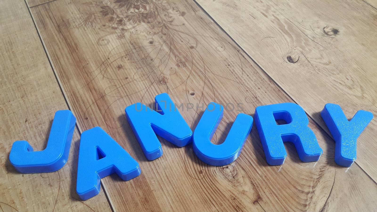 Plastic colored alphabets making words January are placed on a wooden floor. These plastic letters can be used for teaching kids.