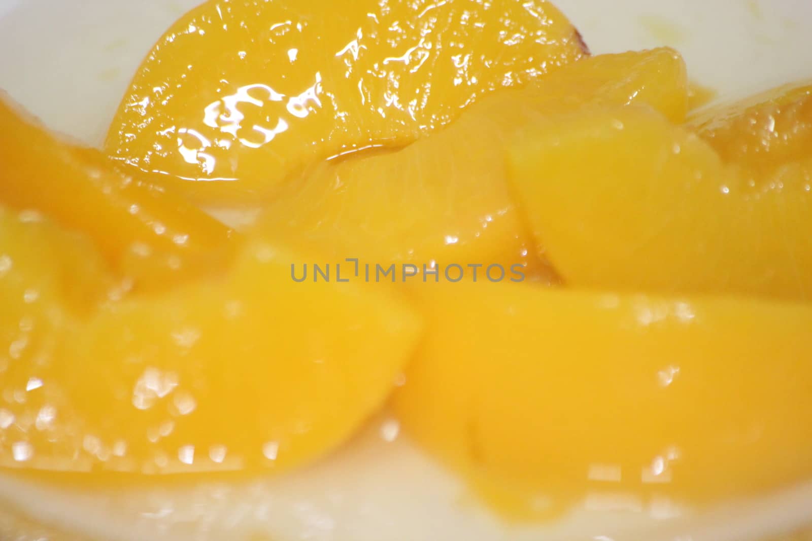 Closeup high angle view with selective focus of yellow peaches slices. Canned peaches halves sprinkled with syrup in white plate.