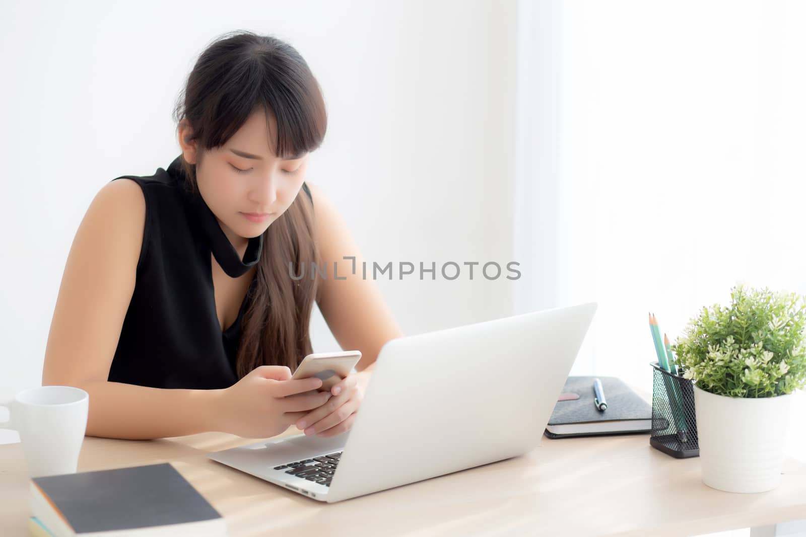 Beautiful young asian woman working laptop computer online to internet and texting message on smart mobile phone, freelance using notebook, business and communication concept.