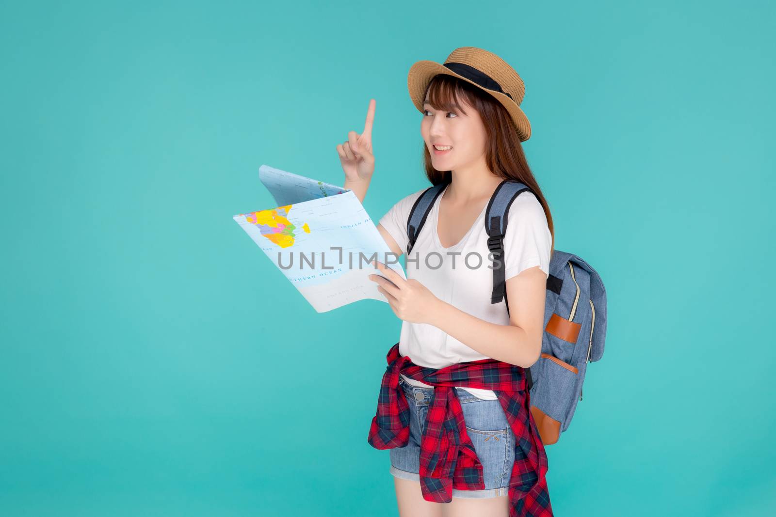 Beautiful happy young asian woman travel holding and looking a paper map isolated on blue background, asia girl pointing and search journey with direction in vacation trip with cheerful for leisure.