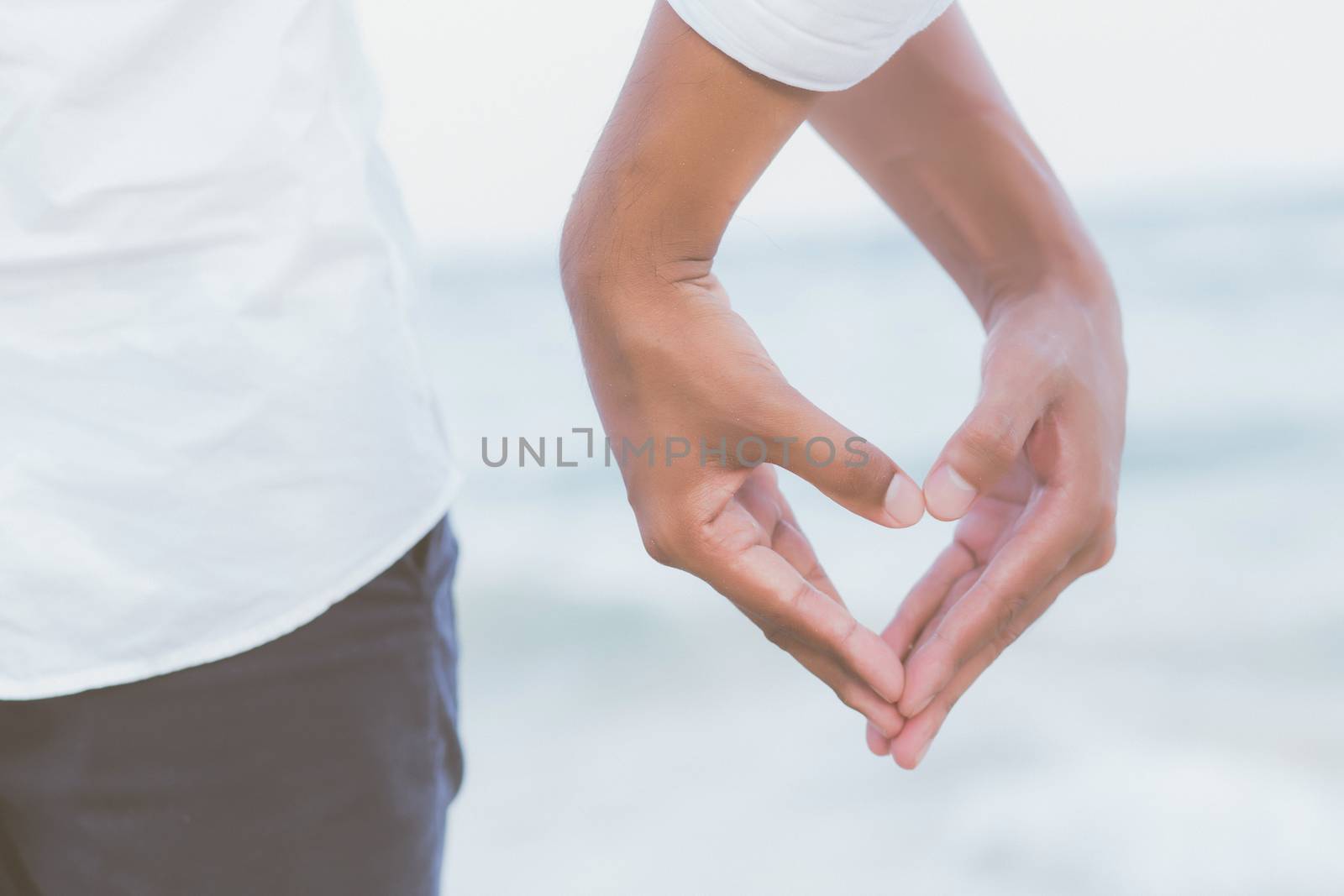 Closeup hand heart shape of young couple gay holding together on the beach in summer in vacation, happy asia Homosexual having love, LGBT of relationship legal and valentine day concept.