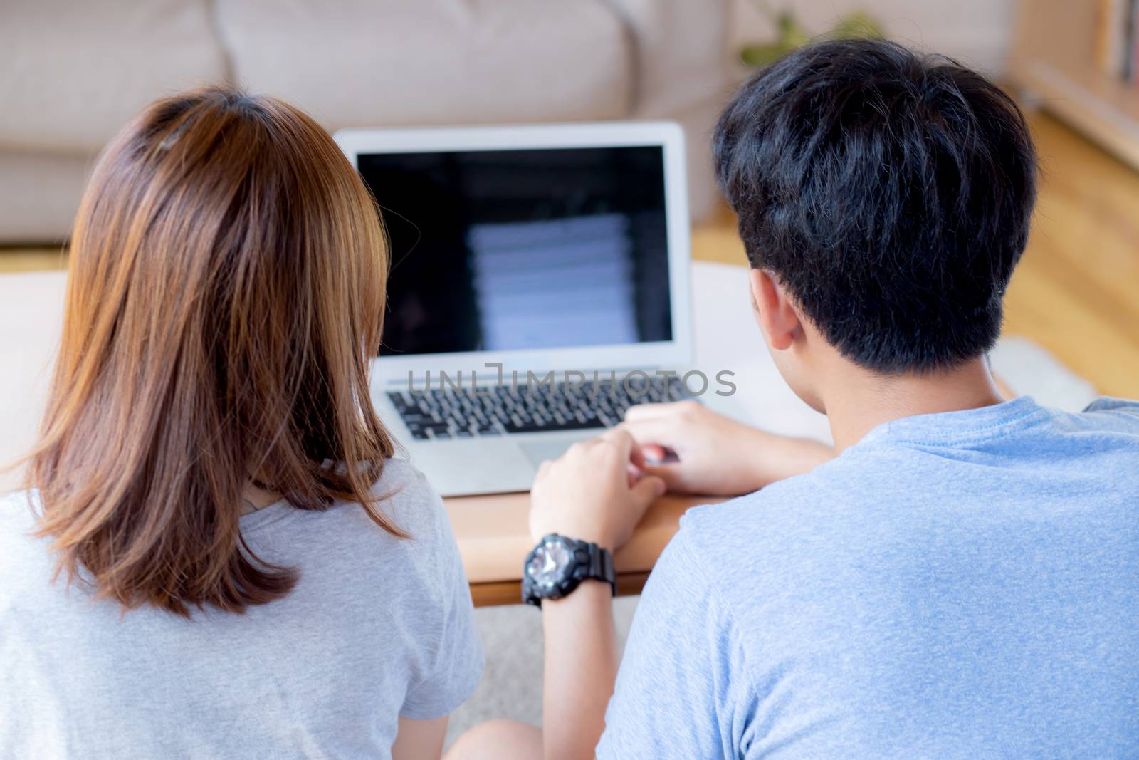 Back view of young asian couple working laptop with blank screen display, family planning and searching content together, man and woman looking computer, business and communication concept.