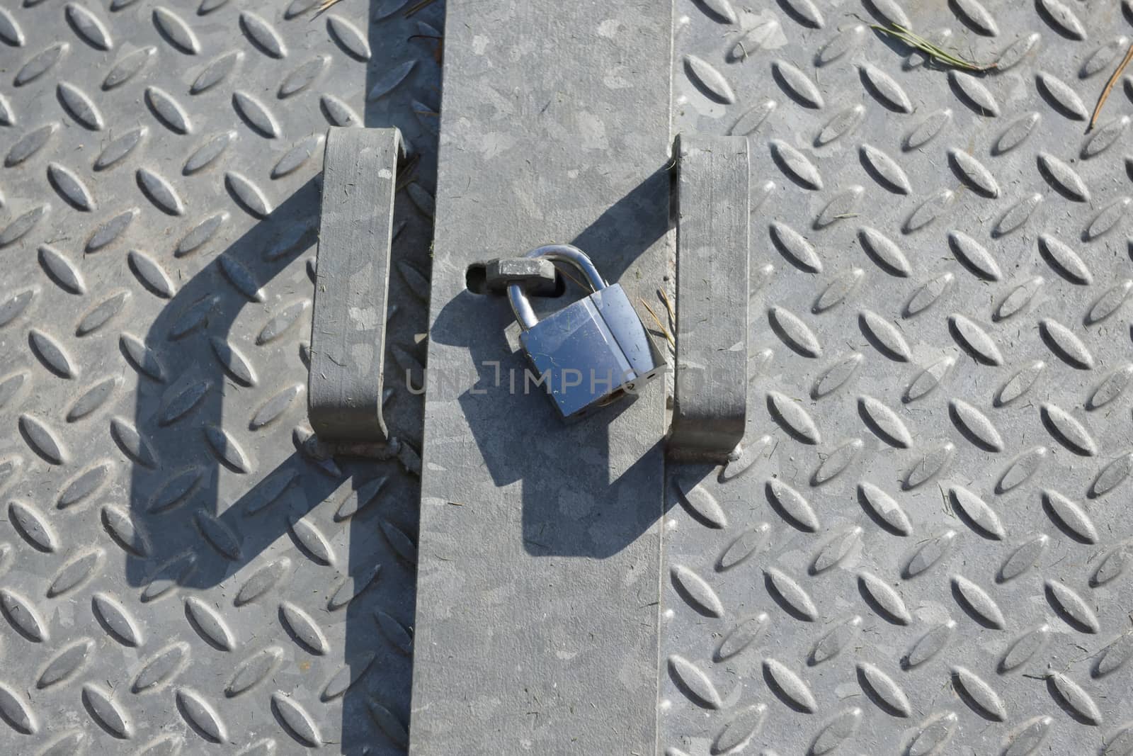 Checkered diamond patterned galvanized steel plates, lit by natural sunlight in an outdoor setting. Shiny metal padlock sits between the two handles