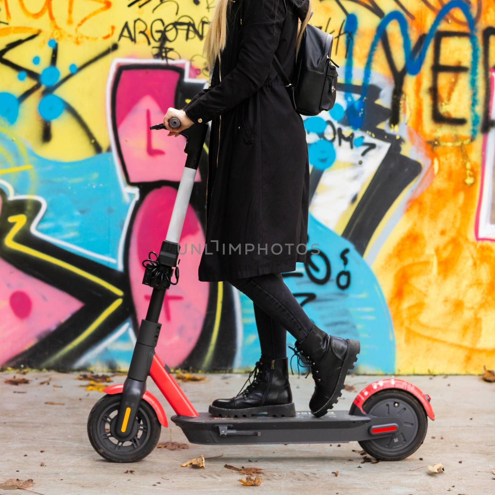 Trendy teenage girl riding public rental electric scooter in urban city environment at fall. New eco-friendly modern public city transport in Ljubljana by kasto