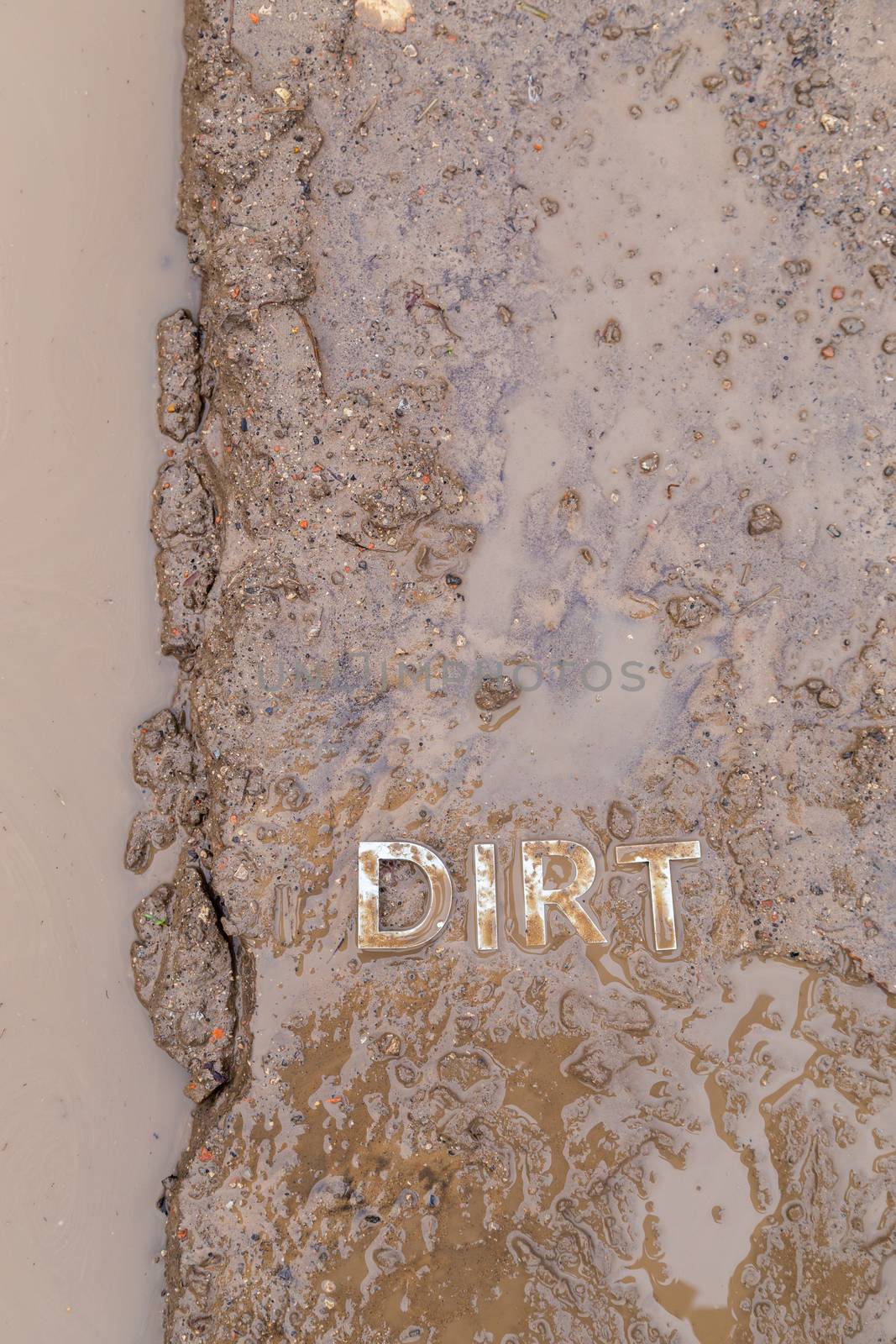 the word mud imprinted in wet dirt road surface and puddle - close-up with selective focus in flat lay perspective.