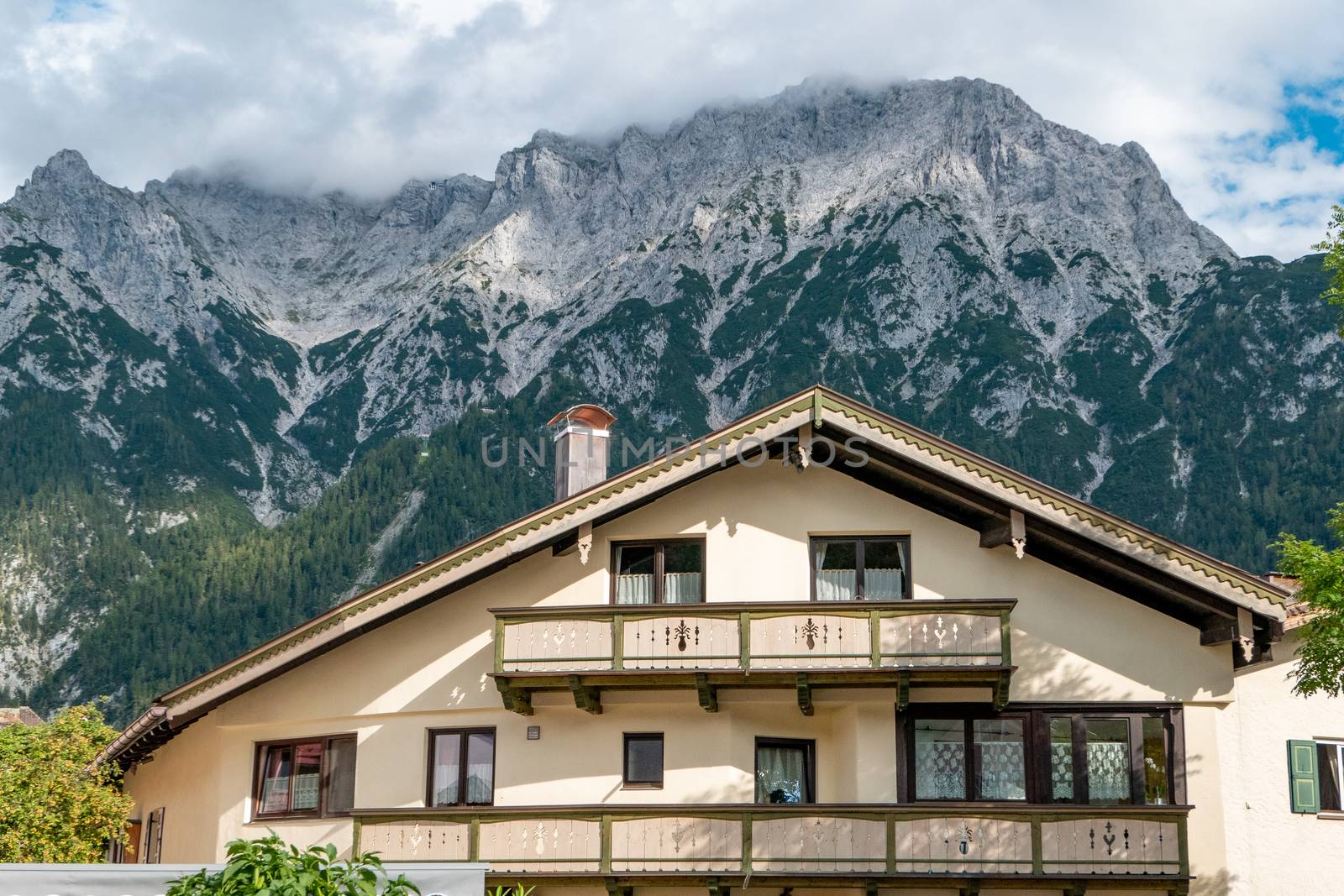 Mittenwald, Bavaria/Germany - 15.08.2020: A big beautiful house with balcony and many windows in front of a huge mountain range, which is lost in clouds.