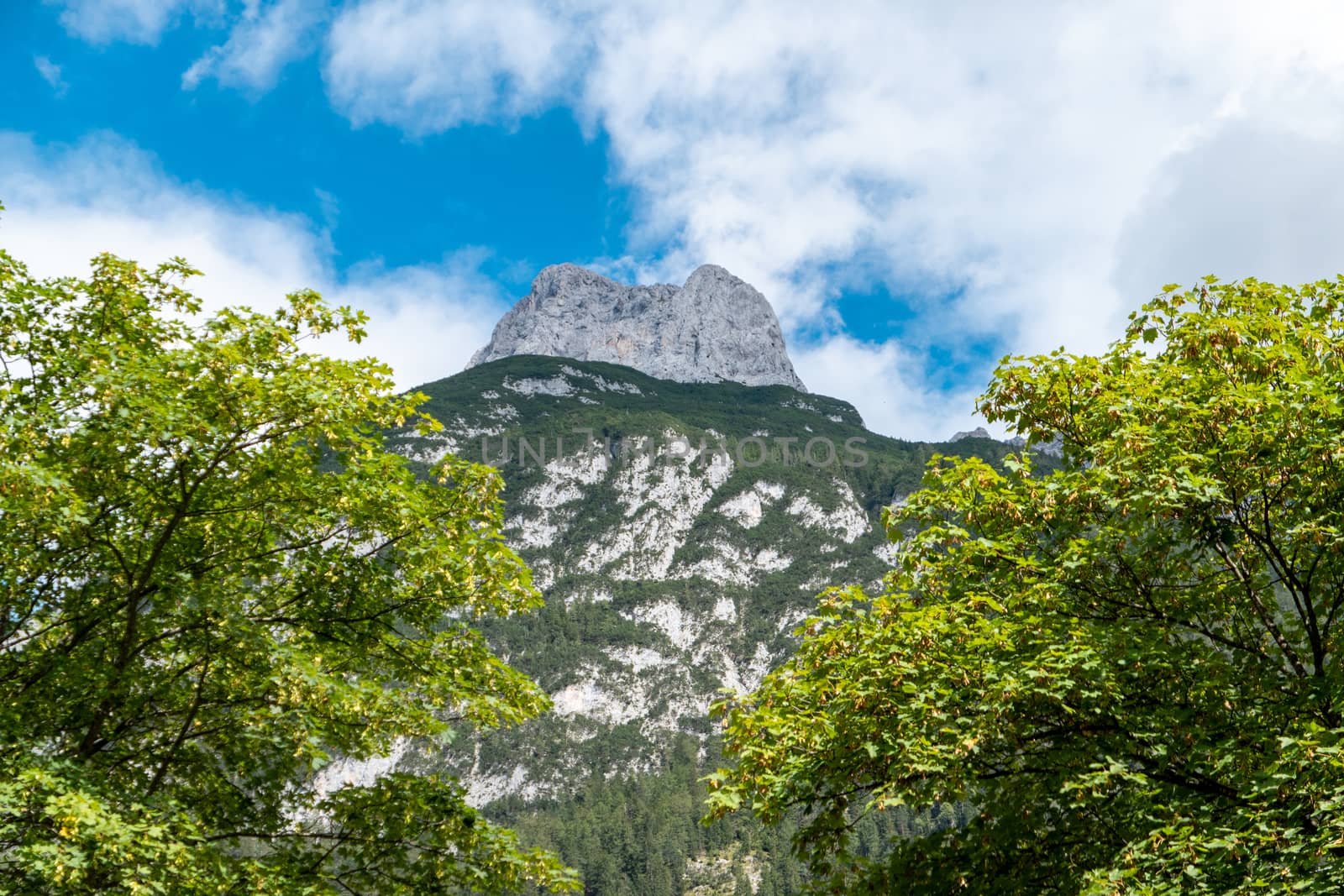 The view through two trees to a mountain with a blue sky and clouds in Mittenwald in Bavaria